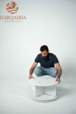 a man setuping white rotatable shoe storage contains decorative plants with a white background and logo barqasha